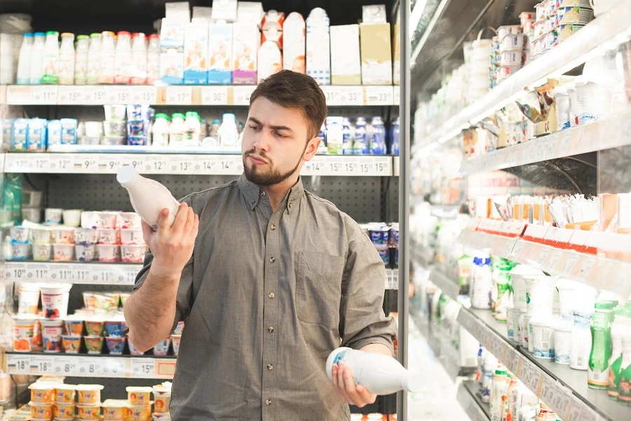 bearded man looks at yogurt bottle label in supermarket